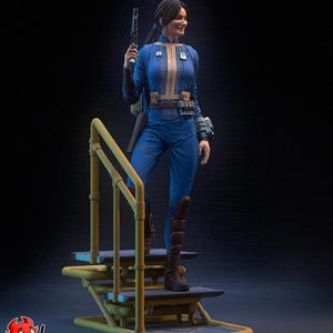 Op de afbeelding: Gedetailleerd beeldje van een vrouw in een blauwe overall, met een blaster. Ze staat op een geel en grijs platform met een reling. Het figuur heeft bruine laarzen en een gereedschapsriem. De tekst "PATREON h3LLcreator" is zichtbaar.
