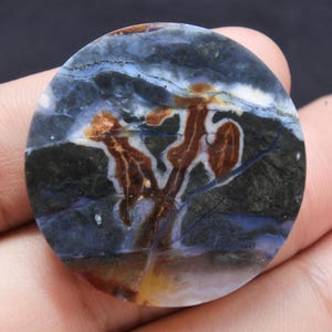 May include: A round, polished stone with a unique pattern. The stone features a blend of dark blue, brown, and white hues, with a striking, tree-like design in the center. The stone's surface is smooth and reflective, showcasing natural variations.