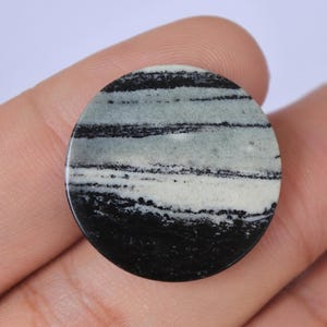 May include: A round, black and white striped cabochon gemstone. The stone has a smooth, polished surface and is approximately 5 cm in diameter.