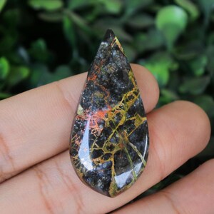May include: A teardrop-shaped pendant made of black, gold, and orange stone with a unique, marbled pattern.