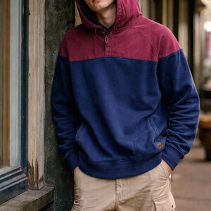 May include: A two-tone hooded sweatshirt in burgundy and navy blue, with a button-up neckline and a kangaroo pocket. The model is wearing khaki cargo pants.