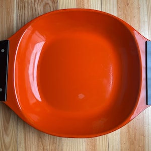 Puede incluir: Plato de servir de cerámica naranja con asas negras. El plato tiene forma ovalada y un acabado brillante.