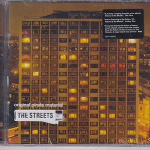 May include: A CD case with a yellow and orange cityscape on the front. The text "original pirate material" and "THE STREETS" is printed on the front of the case.