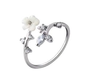 May include: A silver-toned ring featuring a delicate floral design. The ring showcases a white flower and sparkling clear gemstones. The band curves around the finger, with the floral elements adorning the top. A stylish piece of jewelry.