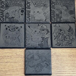 May include: A set of seven gray slate coasters featuring engraved designs from the Pokémon franchise. The coasters depict characters and game box art from various Pokémon versions, including "Blue Version" and "Red Version".