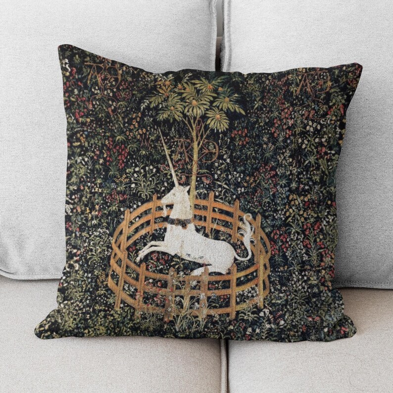 May include: A throw pillow with a tapestry design featuring a white unicorn in a circular fence, surrounded by a lush green forest with colorful flowers.