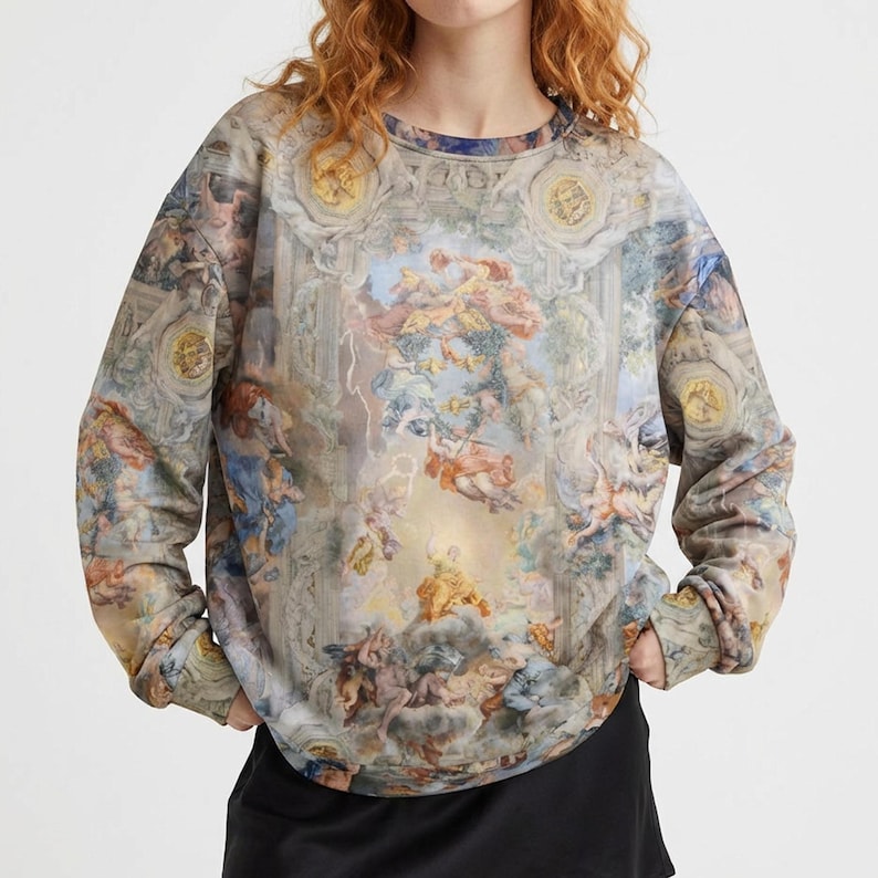 May include: Crew neck sweatshirt featuring a Renaissance-style painting print. The long-sleeved top showcases a detailed depiction of figures, clouds, and architectural elements in shades of beige, blue, and peach. The overall design evokes a classical art aesthetic.