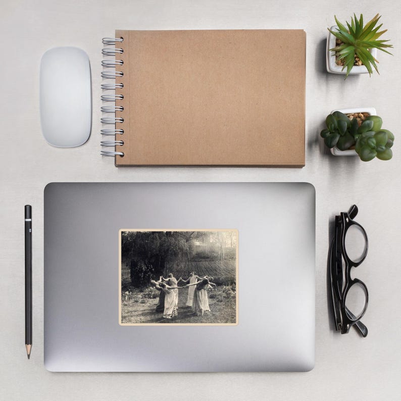 May include: A sticker featuring a sepia-toned image of five figures in flowing dresses holding a long pole, dancing in a circle. The background shows a field and trees. The sticker is on a laptop.