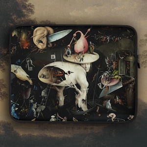 May include: A black laptop sleeve with a print of Hieronymus Bosch's painting "The Garden of Earthly Delights." The artwork shows a surreal landscape with fantastical figures and scenes in a dark, detailed style. The sleeve has a black zip.