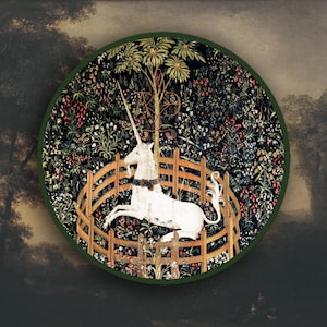 Può includere: Arazzo rotondo con un unicorno bianco all'interno di una recinzione di legno, circondato da un lussureggiante sfondo floreale. L'arazzo ha un bordo verde e una scena di foresta scura e dettagliata sullo sfondo. L'unicorno ha un lungo corno.
