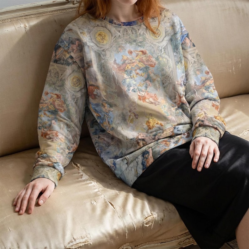 May include: A crew neck sweatshirt with a Renaissance-style painting print in shades of blue, beige, and peach. The long-sleeved top features a detailed design reminiscent of classical art, offering a unique and artistic aesthetic.