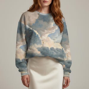 Puede incluir: Una sudadera de cuello redondo con un diseño de cielo nublado en tonos azules, blancos y beige. La parte superior de manga larga tiene puños acanalados y un ajuste relajado. La sudadera está hecha de un material suave.