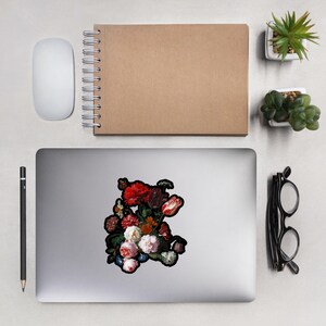 Pu&ograve; includere: Un adesivo per laptop con una natura morta floreale, con fiori rossi, bianchi e rosa. L'adesivo ha un bordo nero. Un mouse bianco, un taccuino marrone, una matita e un paio di occhiali sono anche sulla scrivania.