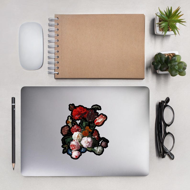 Pu&ograve; includere: Un adesivo per laptop con una natura morta floreale, con fiori rossi, bianchi e rosa. L'adesivo ha un bordo nero. Un mouse bianco, un taccuino marrone, una matita e un paio di occhiali sono anche sulla scrivania.