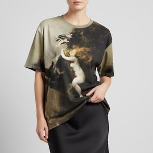 May include: Olive green short-sleeve t-shirt featuring a classical painting print. The artwork depicts a nude woman with flowing red hair embracing a dark, shadowy figure. The shirt has a crew neck and a relaxed fit.
