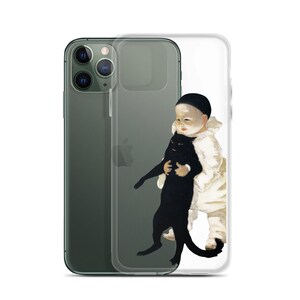 以下が含まれることがあります： 白い服と黒い帽子をかぶった子供が黒猫を抱いている絵が描かれた透明なiPhoneケース。ケースは緑色のiPhoneに装着されています。