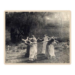 May include: A vintage black and white photograph depicts a group of people in long dresses holding hands in a circle. They are in a grassy area with trees and flowers in the background. The image has a sepia tone.