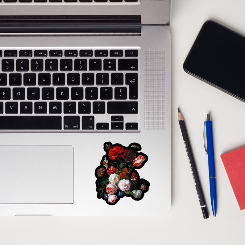 Pu&ograve; includere: Un adesivo floreale con un bouquet di fiori rossi, rosa e bianchi con foglie verdi. L'adesivo &egrave; su un laptop, accanto a una matita nera, una penna blu e un blocco note rosso. I fiori hanno uno sfondo scuro.