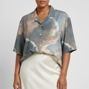 May include: Short-sleeved button-down shirt with a cloudscape print in shades of blue, beige, and white. The shirt has a classic collar and a relaxed fit, suitable for casual wear. The fabric appears soft and lightweight.