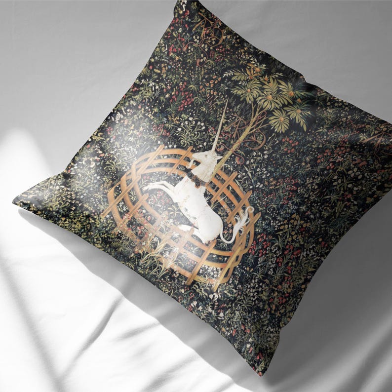 May include: A throw pillow with a tapestry design featuring a white unicorn trapped in a circular wooden fence. The background is a dark green forest with a variety of flowers and leaves.