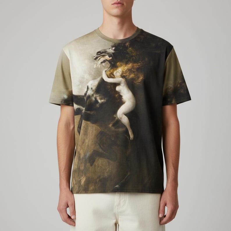 May include: A short-sleeved t-shirt featuring a classical painting of a woman riding a horse. The artwork is in shades of brown, beige, and olive green. The woman has long, flowing red hair. The shirt has a crew neck and a relaxed fit.
