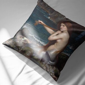 Puede incluir: Una pintura de una sirena con el pelo largo y rojo, sentada en las rocas junto al mar. Est&aacute; sujetando un mech&oacute;n de pelo en la mano y mirando hacia un lado. El mar es de un color azul oscuro y hay olas rompiendo contra las rocas.