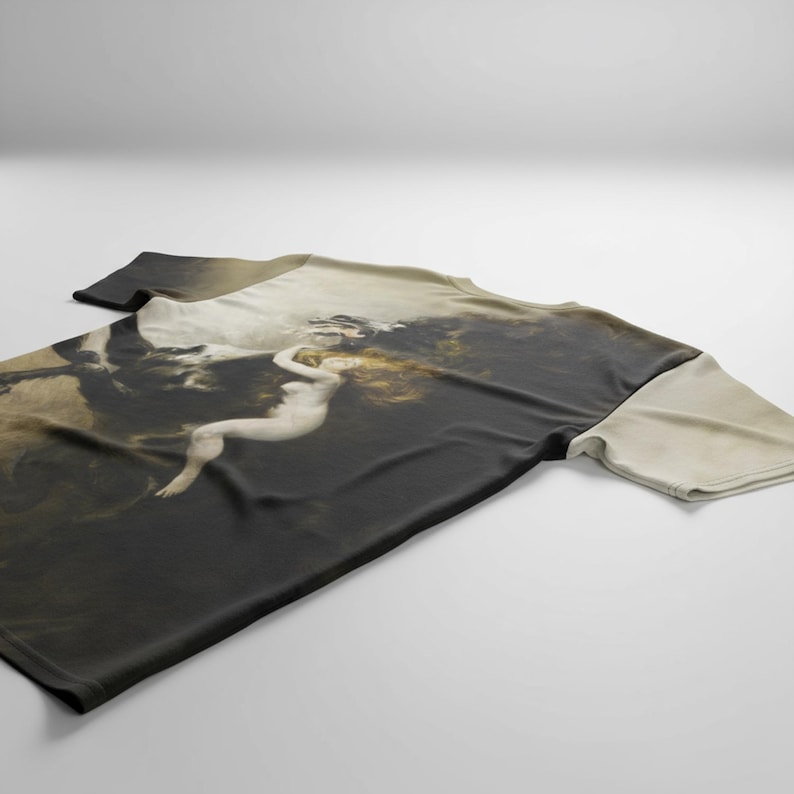 May include: A short-sleeved t-shirt featuring a classical painting of a nude figure with long hair. The artwork is predominantly dark with lighter shades of beige and white, creating a dramatic contrast. The shirt is laid flat on a white surface.