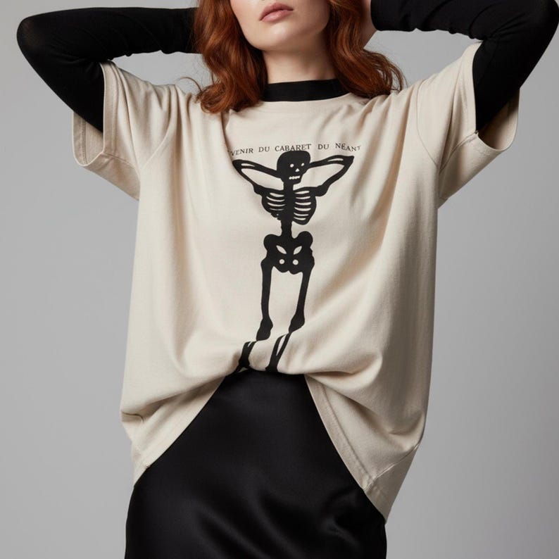 Puede incluir: Camiseta beige con un gr&aacute;fico de esqueleto negro y el texto "VENIR DU CABARET DU NEANT". La camiseta tiene cuello negro y mangas largas. La camiseta est&aacute; hecha de un material suave y c&oacute;modo.