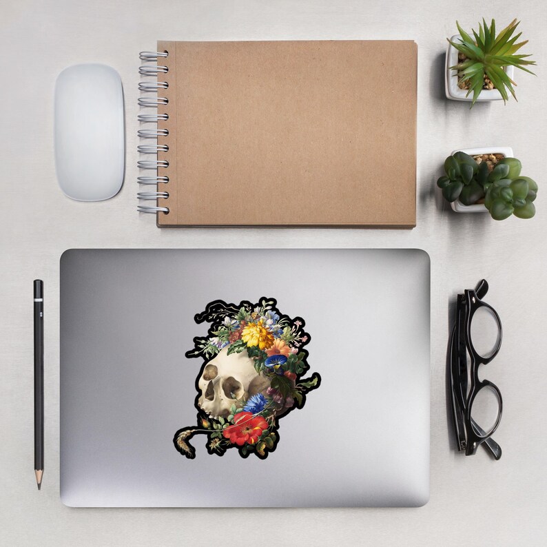 May include: A white skull with a crown of colorful flowers, including red, yellow, and blue, on a black background.