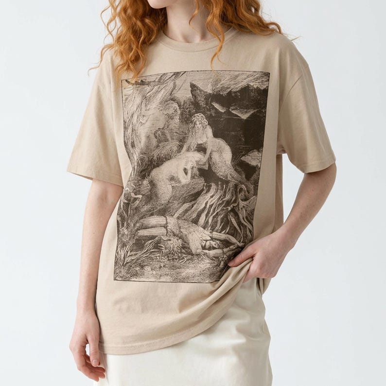 Pu&ograve; includere: T-shirt beige con stampa grafica color seppia. La grafica raffigura un'illustrazione classica e dettagliata di figure in un ambiente naturale. La maglietta ha maniche corte e una vestibilit&agrave; ampia.
