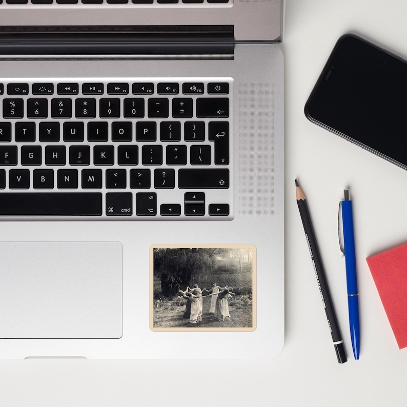 May include: A sticker featuring a black and white image of a group of people dancing in a circle outdoors. The sticker is rectangular with a cream-colored border and is placed on a laptop.