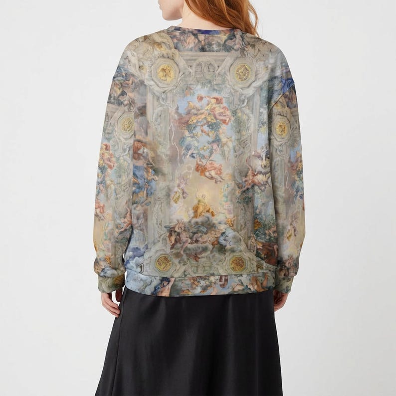 May include: A long-sleeved sweatshirt featuring a Renaissance-style fresco print in shades of blue, beige, and peach. The artwork depicts cherubs, architectural details, and celestial elements. The sweatshirt is paired with a black skirt.