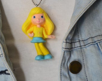 Figura de muñeca de plástico convertida en colgante, collar de muñeca y artículo reciclado de tienda de segunda mano.