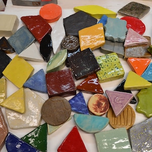 May include: A collection of colorful ceramic tiles in various shapes and sizes, including squares, rectangles, triangles, and circles. The tiles are glazed in a variety of colors, including red, green, blue, yellow, and orange. Some of the tiles have a speckled or textured surface.
