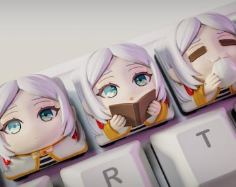 May include: Three white anime-style keycaps with different expressions. The keycaps are on a white keyboard with black keys. The keycaps feature a girl with a book, a girl with a cup, and a girl with a neutral expression.