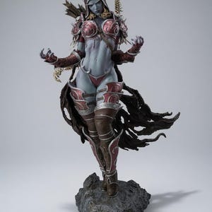 Op de afbeelding: Een gedetailleerd fantasy-figuur met een bleke huid en lange oren, gekleed in een donkerrood en zilverkleurig harnas met een kapmantel. Het figuur staat op een gestructureerde grijze rotsvoet en heeft gedetailleerde bepantsering.