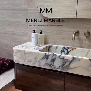 May include: A modern bathroom vanity with a marble countertop and dark wood cabinetry. The countertop features white and gray veining. Two white bottles sit on the counter. The text "MERCI MARBLE" is visible.