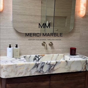 May include: A modern bathroom vanity with a marble sink and dark wood cabinetry. The sink features a white and gray marble pattern. The mirror above has the text "MM MERCI MARBLE CENTURY-OLD STONES, TIMELESS DESIGN".