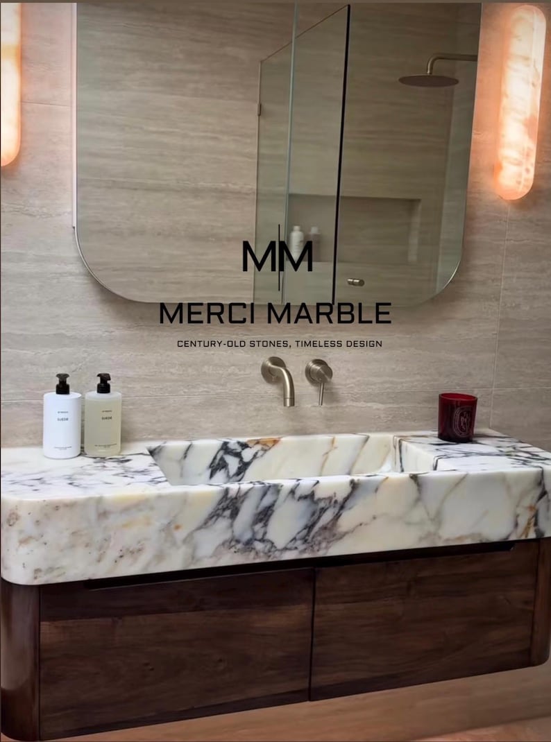 May include: A modern bathroom vanity with a marble sink and dark wood cabinetry. The sink features a white and gray marble pattern. The mirror above has the text "MM MERCI MARBLE CENTURY-OLD STONES, TIMELESS DESIGN".
