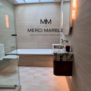 May include: A modern bathroom featuring a bathtub, toilet, and vanity with marble accents. The room has a neutral color palette with a skylight and the text "MERCI MARBLE CENTURY-OLD STONES, TIMELESS DESIGN".