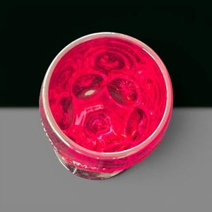 May include: A circular glass vessel featuring a vibrant hot pink hue and a textured, dimpled surface pattern. The interior of the glass displays a repeating series of concave circular indentations that create a distinct visual depth and light refraction.