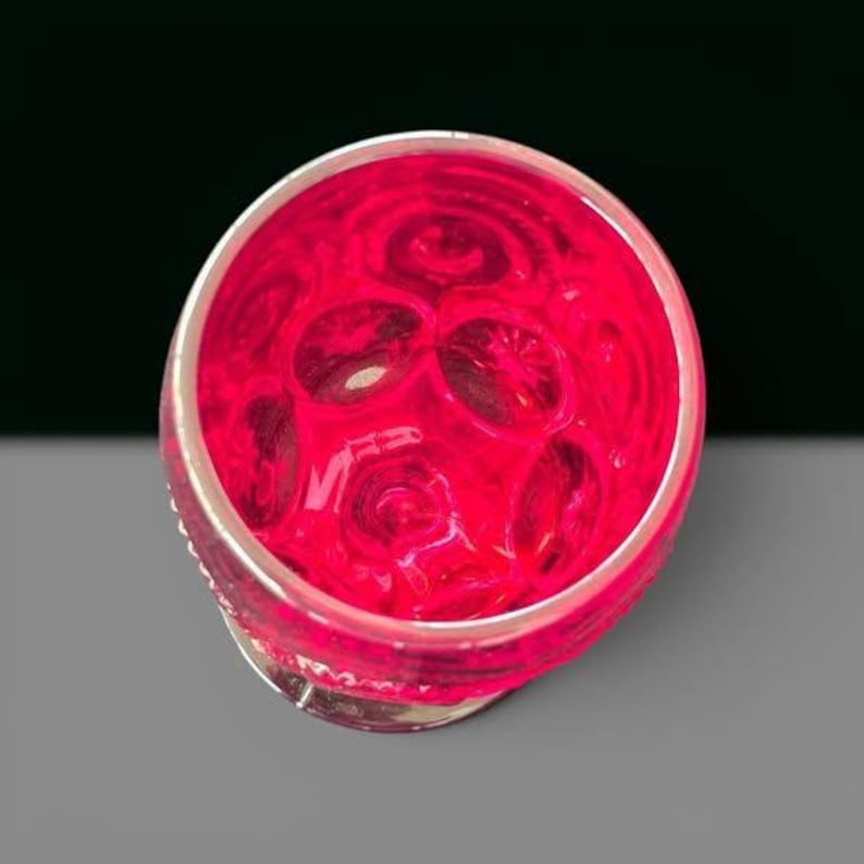 May include: A circular glass vessel featuring a vibrant hot pink hue and a textured, dimpled surface pattern. The interior of the glass displays a repeating series of concave circular indentations that create a distinct visual depth and light refraction.