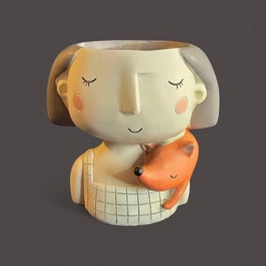 May include: A whimsical ceramic planter shaped like a girl with closed eyes and rosy cheeks, hugging an orange fox. The planter has a grid-like pattern on the front and gray hair. Ideal for small plants or succulents.