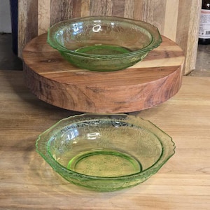 以下が含まれることがあります： 花柄の2つの緑色のガラスボウル。ボウルはスカラップの縁があり、木製の表面に置かれています。ボウルは明るい緑色で、ヴィンテージのようです。