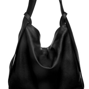 Peut inclure: Un sac hobo noir en cuir texturé, présentant une silhouette souple et non structurée avec une large bandoulière intégrée qui passe à travers les ouvertures supérieures des deux côtés, créant un drapé doux et froncé au centre.