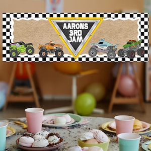 Puede incluir: Una pancarta con un borde a cuadros blanco y negro y un fondo beige. La pancarta presenta cuatro monster trucks y un tri&aacute;ngulo amarillo con el texto "Aarons 3rd Jam". La imagen est&aacute; colocada sobre una mesa con art&iacute;culos de fiesta.