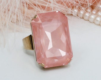 May include: A pink gemstone ring with a gold band. The gemstone is a large, faceted, rectangular shape.