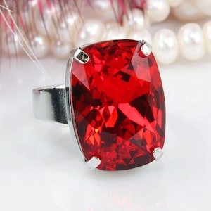 May include: A silver ring with a large, red, cushion-cut gemstone.