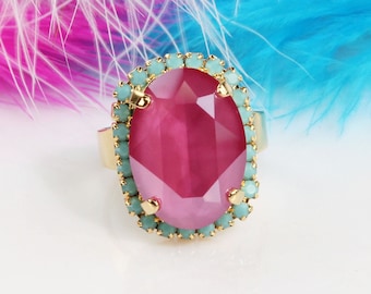 May include: A gold ring with a large pink oval-shaped gemstone surrounded by a halo of light blue rhinestones.