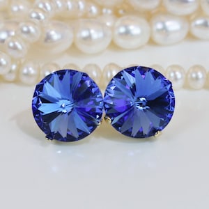 May include: A pair of blue crystal earrings with a faceted design. The earrings are round and have a gold setting.